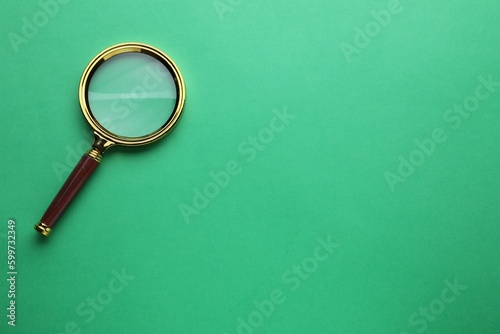 Magnifying glass on green background, top view. Space for text