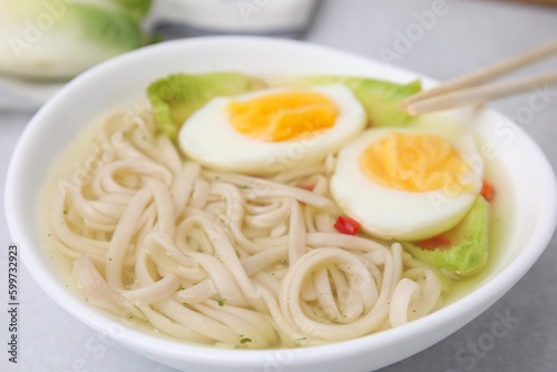 Bowl of delicious rice noodle soup with celery and egg on light grey table, closeup