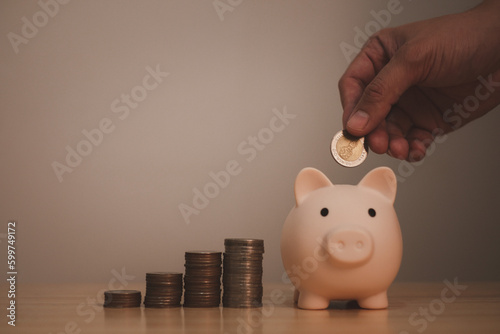 piggy bank with hand of a man under saving coin in piggy bank, symbol of saving for future investment or retirement by small deposit money continuously
