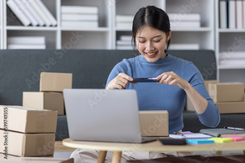 Asian business woman on sofa using a laptop computer checking customer order online shipping boxes at home. Starting SME Small business entrepreneur freelance. Online business, SME Work home concept. 