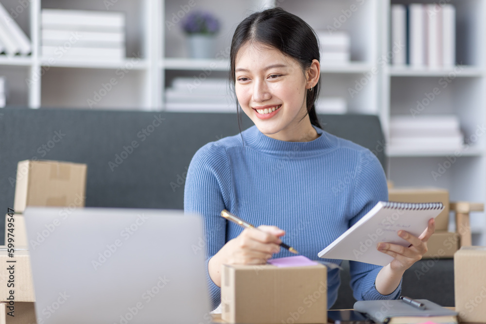 Asian business woman on sofa using a laptop computer checking customer order online shipping boxes at home. Starting SME Small business entrepreneur freelance. Online business, SME Work home concept.
Asian business woman on sofa using a laptop computer checking customer order online shipping boxes at home. Starting SME Small business entrepreneur freelance. Online business, SME Work home concept.