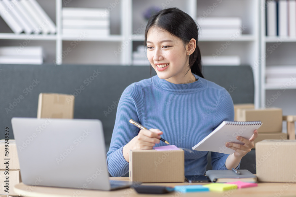 Asian business woman on sofa using a laptop computer checking customer order online shipping boxes at home. Starting SME Small business entrepreneur freelance. Online business, SME Work home concept.
