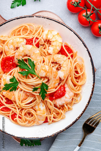 Prepared spaghetti pasta with shrimp, red tomatoes, olive oil and parsley on gray background. Top view, close-up