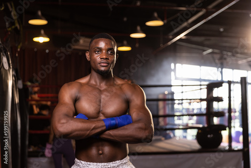 Young confident African American boxer standing in pose and ready to fight, stadium background.