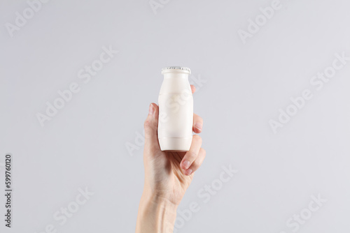 Female hand holding a bottle of yogurt on a gray background