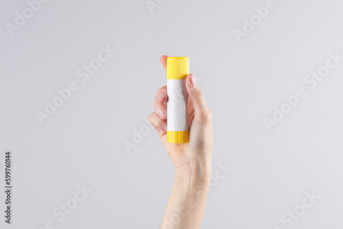 Female hand holding paper glue stick on gray background