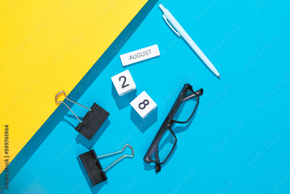 White cube calendar with the date august 28 with stationery, or office accessories on a blue yellow background. Deadline, planning, business concept White cube calendar with the date august 28 with stationery, or office accessories on a blue yellow background. Deadline, planning, business concept