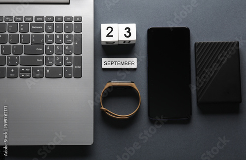White wooden block calendar with date september 23 and modern gadgets on gray background. Top view
