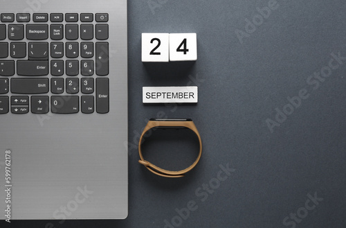 White wooden block calendar with date september 24 and laptop with smart bracelet on gray background. Business, deadline, planning, Flat lay