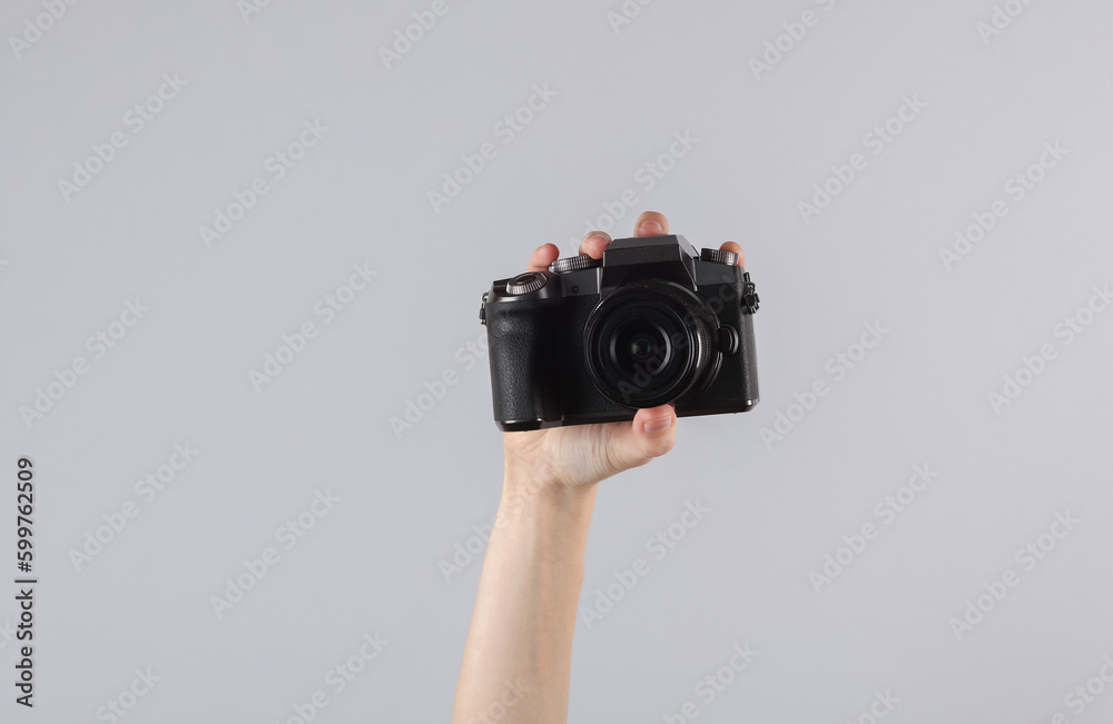 Woman's hand holding a modern digital camera on gray background