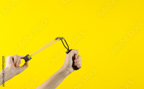 Fotografiet Hand holding a slingshot on a yellow background