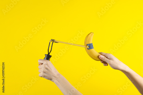 Hands holding slingshot with banana on a yellow background photo
