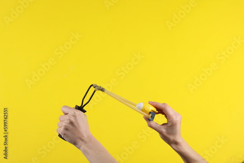 Bilde på lerret Hands holding slingshot with toy space shuttle rocket on a yellow background