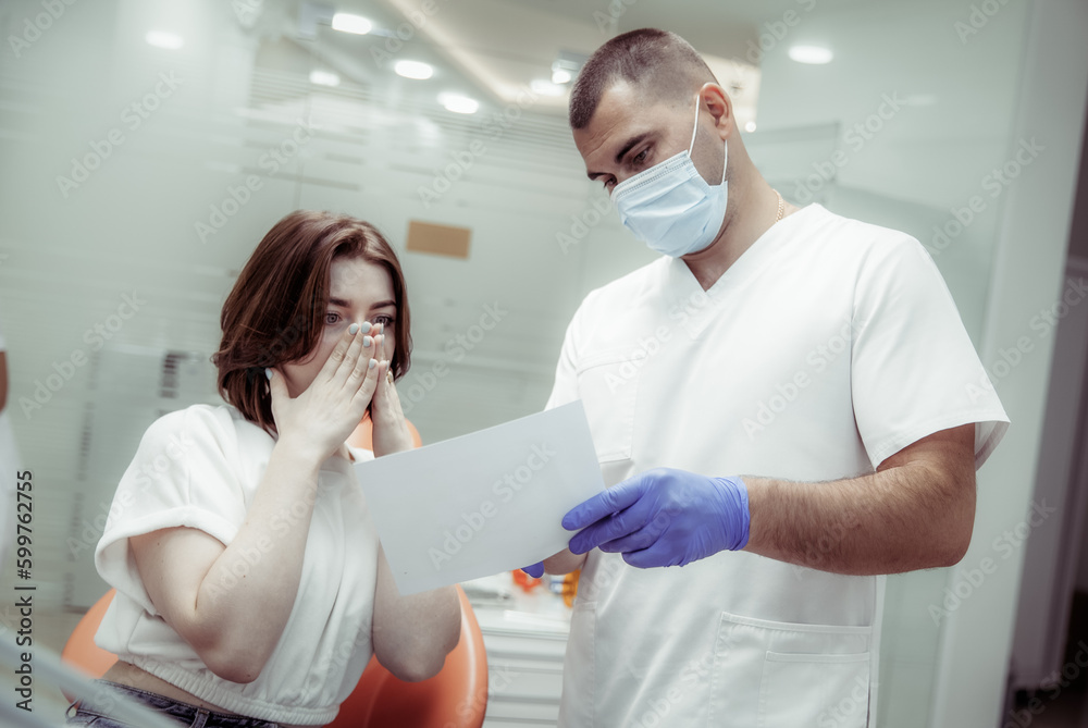 Obraz premium Professional doctor dentist showing a picture of teeth to a terrified woman patient