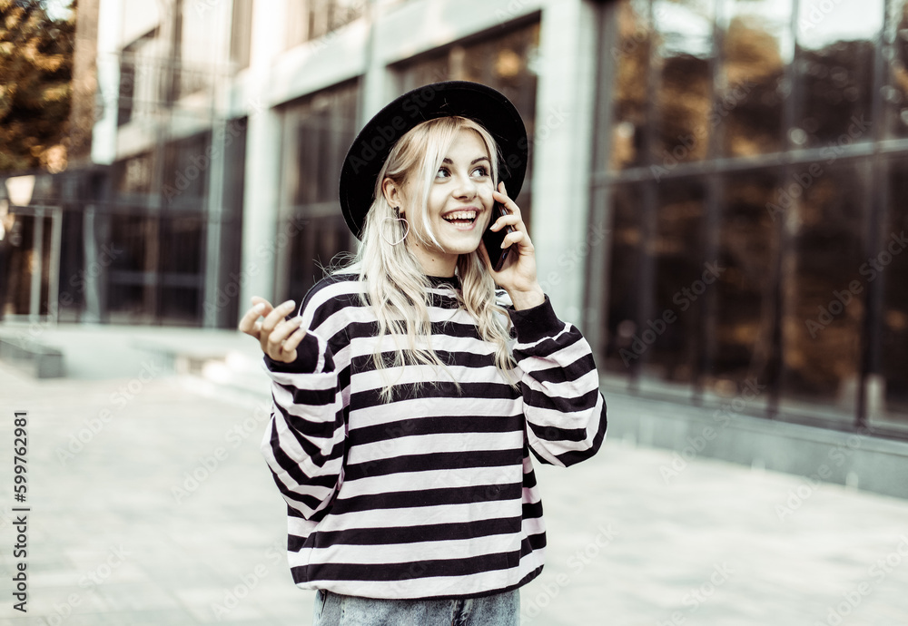 Young charismatic smiling woman in hat talking on the phone outdoors