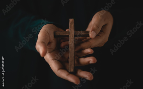 Spirituality, Religion and Hope Concept. Person with Wooden Cross on Hands. Symbol of Humility, Supplication, Believe and Faith for Christian People. Dark Tone. Cropped and Selective focus