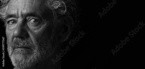Black and white portrait of an attractive older Caucasian man with grey hair and beard. Turned to the right side with a serious or pensive expression. Room for copy.