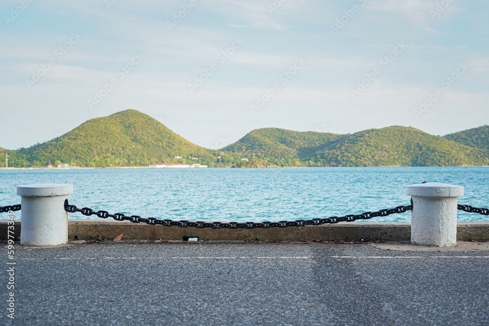 Roadside iron chain and cement pillar fence at the edge of bay route with beautiful island view. Transportation structure with nature photo, selective focus.