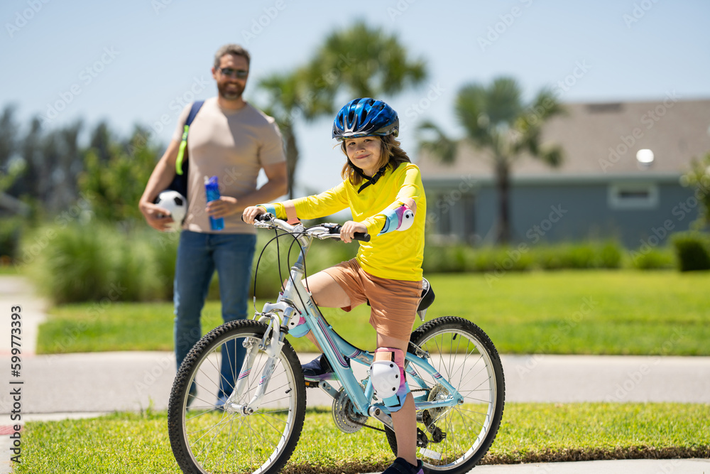 Father and son in bike helmet for learning to ride bicycle at park. Father helping son cycling. Father and son on the bicycle on summer day. Little son trying to ride bike with father. Fathers day. Father and son in bike helmet for learning to ride bicycle at park. Father helping son cycling. Father and son on the bicycle on summer day. Little son trying to ride bike with father. Fathers day.