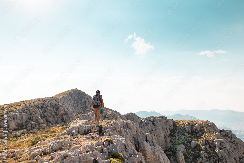 two girls with backpacks walk along a mountain path.
