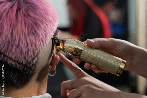 The hairdresser shaves the back of the head of a female client. Rear view of a woman with short pink hair in a barbershop.