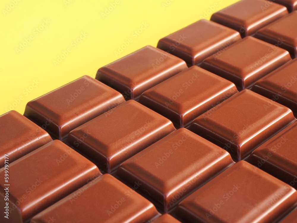 Close up of a milk chocolate bar on a yellow background Close up of a milk chocolate bar on a yellow background