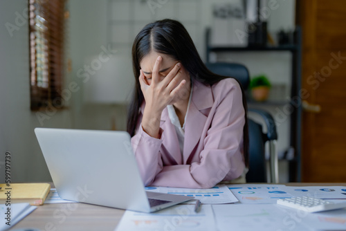 Fotografia Portrait of a young Asian woman showing acute headache from sitting for a long time at work