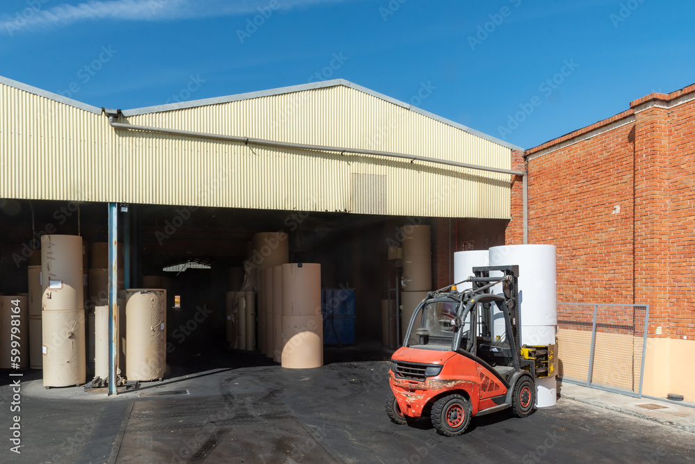 Forklift with clamps to move reels of paper in a warehouse of a paper industry. Forklift with clamps to move reels of paper in a warehouse of a paper industry.