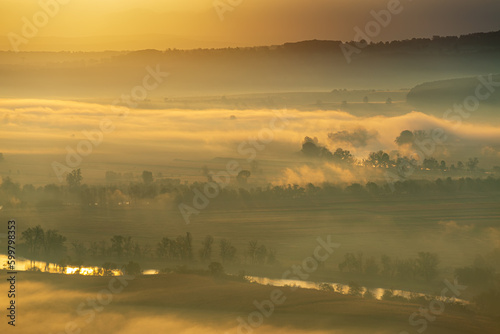 Aerial view of the valley in early morning mist  beautiful in the highlands. Low clouds and fog cover the sleeping meadow. Alpine mountain valley mists landscape at dawn. Serene moment in rural area