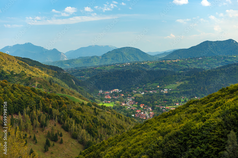 Fototapeta premium Rural idyllic landscape of the small villages in the Rucar-Bran mountain area, Brasov, Romania, scattered on the wooded hills, with the Bucegi mountains in the background, in wonderful springtime day