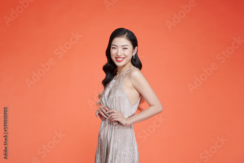 Sensual asian woman with beautiful wavy hairs in beige shiny dress posing over red background