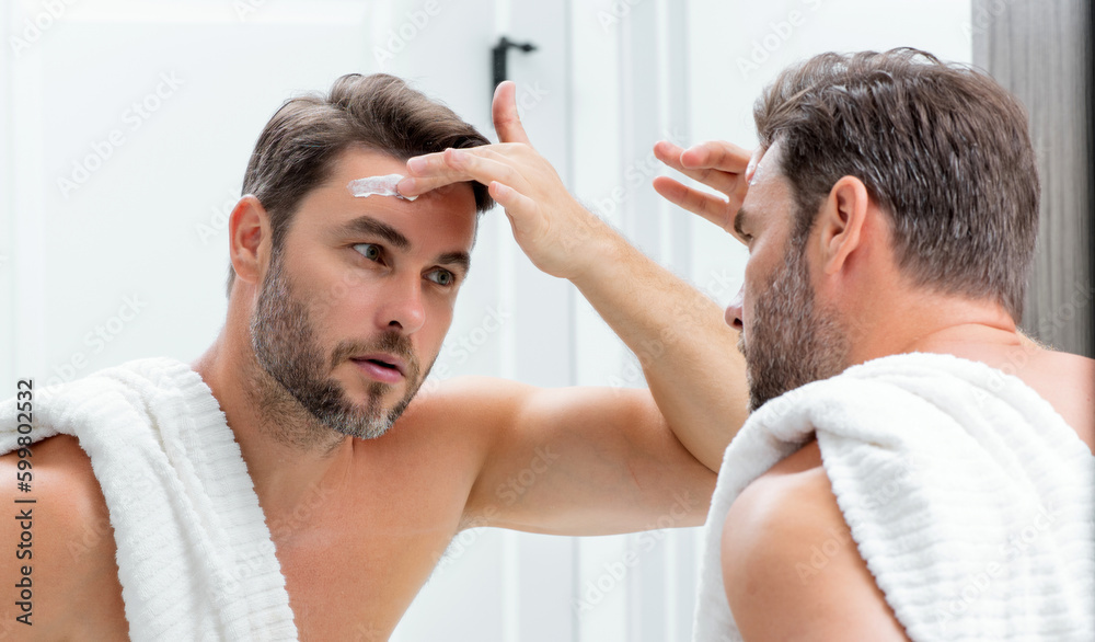 Fototapeta premium Close-up male wrinkles. Portrait of brunet man touching skin wrinkles. Middle aged man with touch wrinkles in front of the mirror. Aged skin. Man 40s cosmetic, skin treatment. Male face with wrinkles.