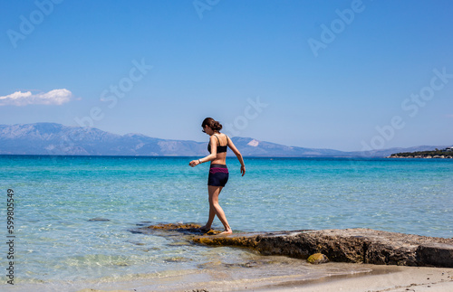 Young beautiful woman in swimming clothes goes to the sea direction on rocks 
