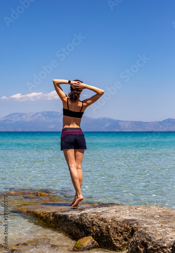 Beautiful body young Woman practicing yoga on a rock in front of the sea, healthy lifestyle, travel, sport concept, vertical 