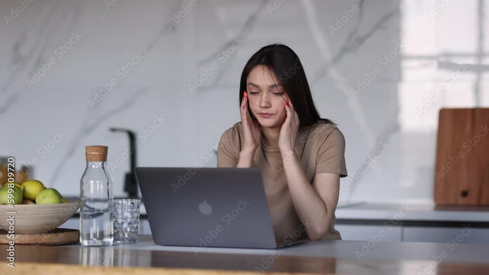 Young tired woman working on laptop in the kitchen Young tired woman working on laptop in the kitchen