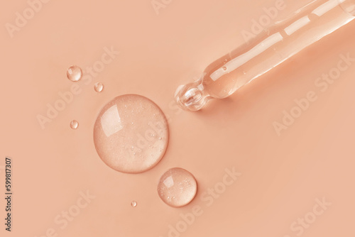 The gel dripping from the dropper is transparent in the form of round droplets on a beige background.