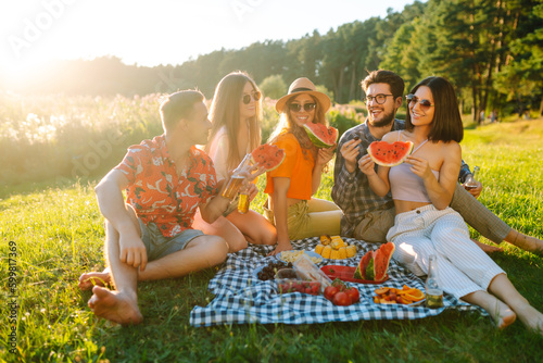 Happy groop of friend resting in nature in the picnic drinking beer, cheers. People, lifestyle, relaxation and vacations concept.