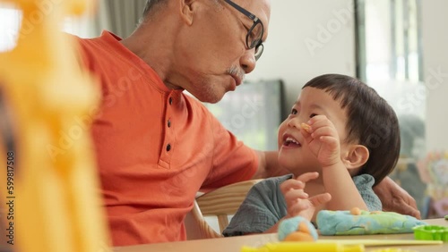 Portrait of Asian Grandfather playing with his Grandson while making toys from plasticine at home. Chinese Senior man and Little child boy playing dough. Creativity and hobby.	