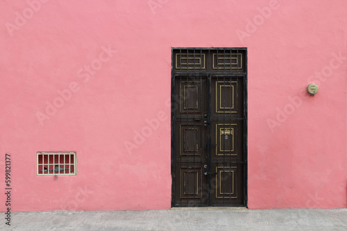 The facade of the building is painted pink with a brown front door. Colonial style of Mexican architecture.