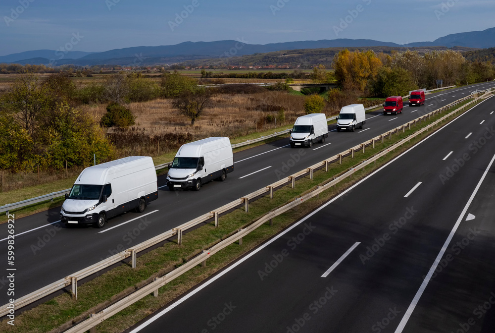 White and red minivans are moving in a convoy on the highway.  White and red modern delivery small shipment cargo courier van moving fast on motorway road to city urban suburb.