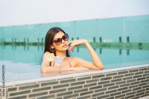 Portait of Beautiful Asian girl wearing sunglass with tropical cocktail and enjoying sunny weather at outdoor swimming pool. People Lifestyle, Freedom, vacation, travel, summertime concept photo