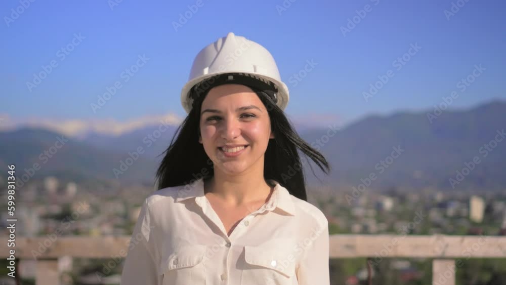 Young architect in helmet, engineer, designer, clerk, white woman. Girl at construction site smiling at camera. Portrait against blue sky, city and mountains. Beautiful and happy developer. Young architect in helmet, engineer, designer, clerk, white woman. Girl at construction site smiling at camera. Portrait against blue sky, city and mountains. Beautiful and happy developer.