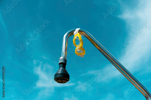 Yellow pool goggles hanging from a pool shower with blue sky in the background. Summer concept. Aesthetic summer.