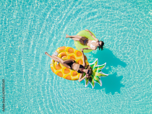 Aerial drone view of girls in swimming pool from above, happy kids swim on inflatable ring donut and mattress, girls have fun in water on family vacation on holiday resort