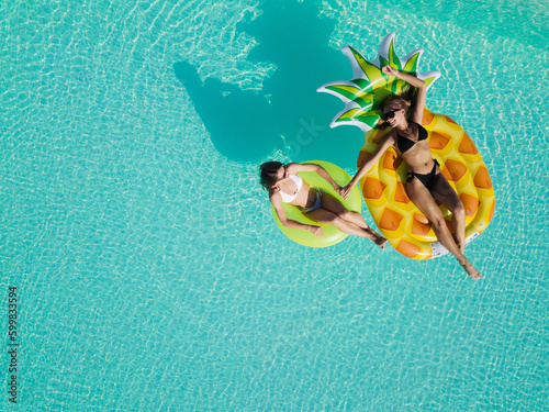 Aerial drone view of girls in swimming pool from above, happy kids swim on inflatable ring donut and mattress, girls have fun in water on family vacation on holiday resort