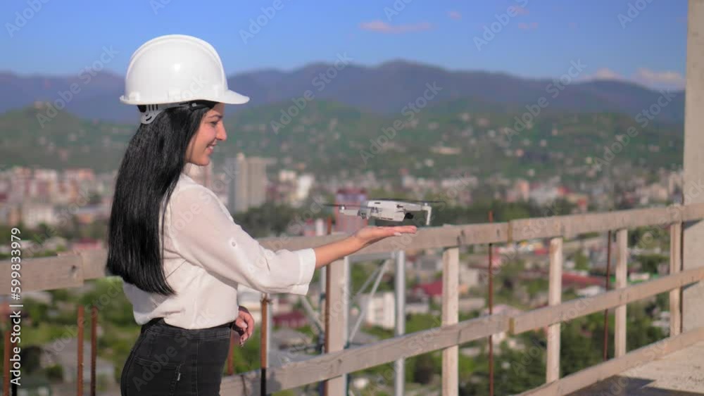 Surveyor engineer launched drone to inspect structure from bird's eye view at project's construction site. Young woman working in construction uses drone, antenna, wearing white helmet Surveyor engineer launched drone to inspect structure from bird's eye view at project's construction site. Young woman working in construction uses drone, antenna, wearing white helmet