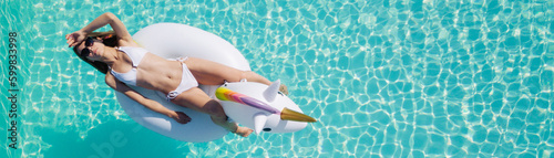Young beautiful brown-haired girl with a good figure tan in the pool on an inflatable unicorn in a black swimsuit.