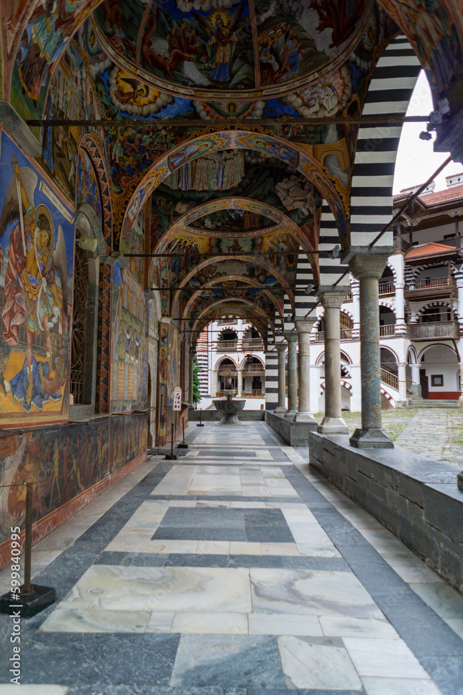 Cloister of the Rila Monastery in Bulgaria, it has many arches and columns, many paintings and frescoes, it is very colorful, photo on a cloudy day.
