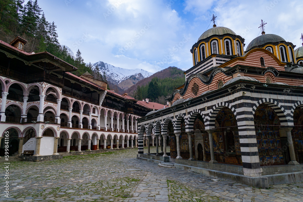 Rila Monastery in Bulgaria, without tourists and without people, on a day with some clouds, and with the snowy mountain in the background.