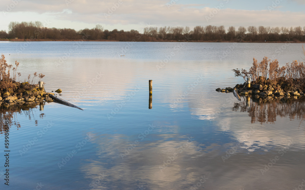 Fototapeta premium clouds reflecting in lake with rock barrier and treeline